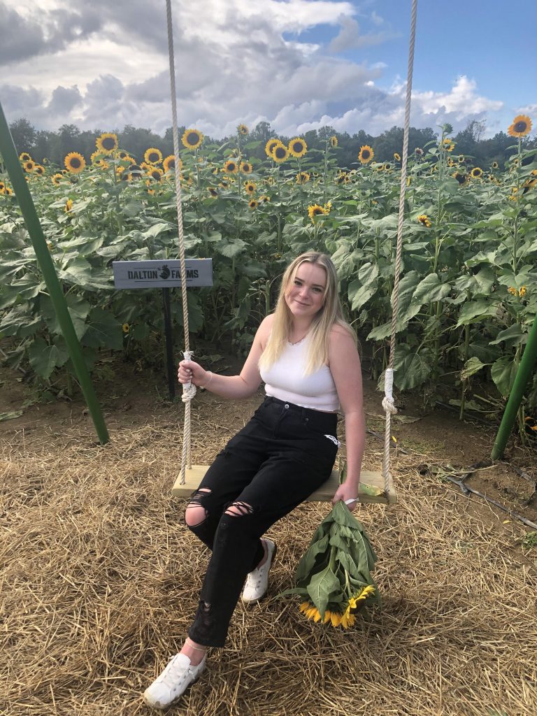 Kristin poses in front of sun flowers on a swing.