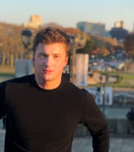 Tyler Weiss poses at a tourist destination, with a city behind him. 