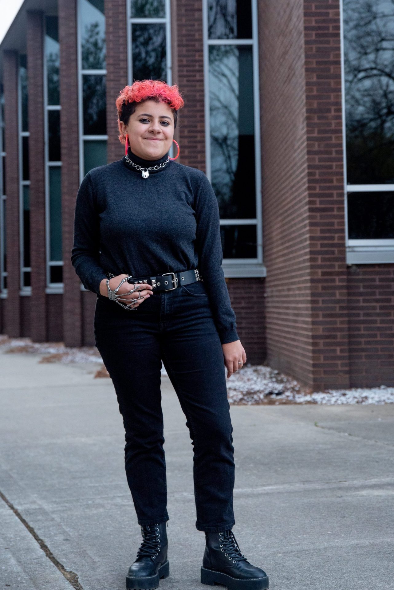 Nyds poses outside of Wilson Hall with bright orange hair that matches their hoop earrings.