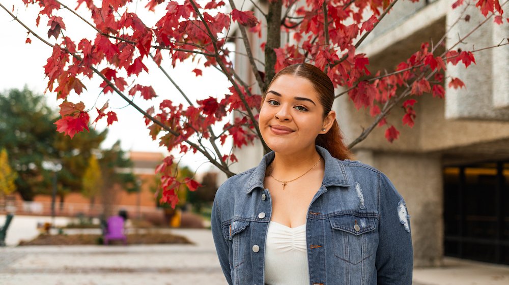 Shirley stands in front of a tree and a nearby academic building.