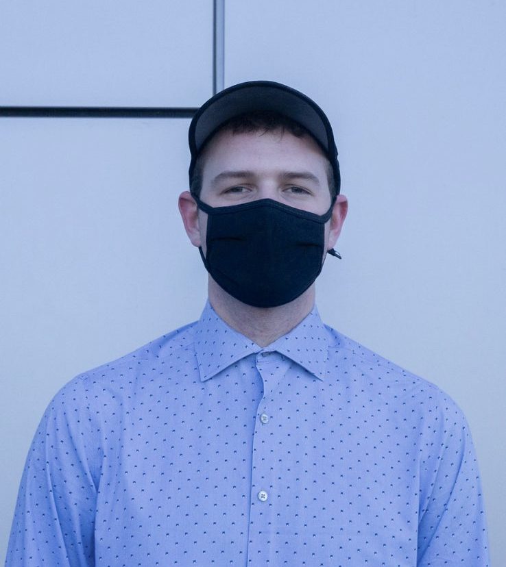 Joseph Laggy stands for a portrait while wearing a blue collared shirt and a black mask for covid. 