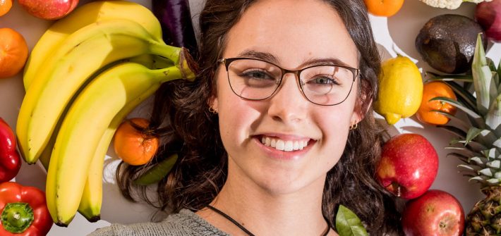 Close of Hannah's face surrounded by fruit.