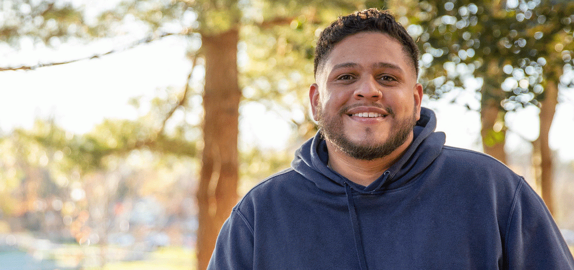 Martin Gonzalez sits by trees on campus.