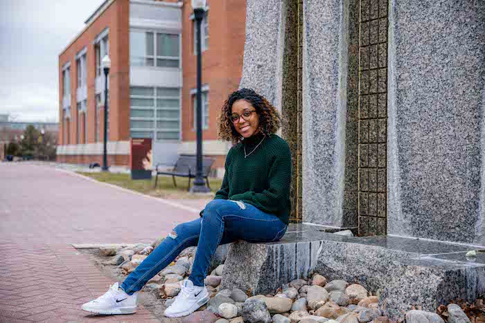 Briana sitting and posing on the fountain stature outside Campbell Library. 