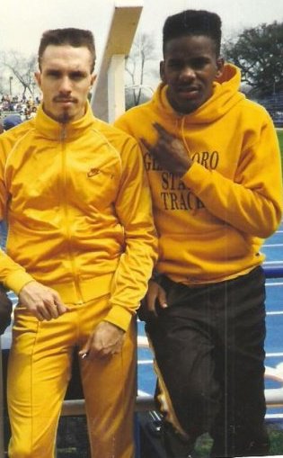 Brad posing with a friend outside the track field while wearing a Glassboro State Track sweatshirt.