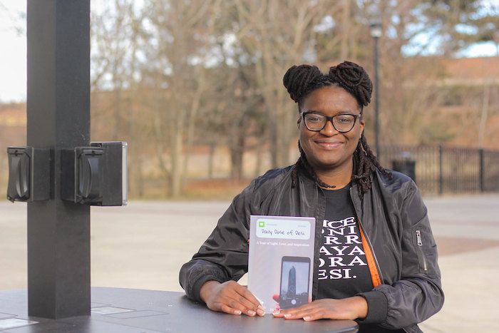 Desi sitting outside the student center holding her book.