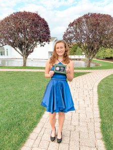 Emma posing for a picture while holding a certificate and wearing a blue dress.