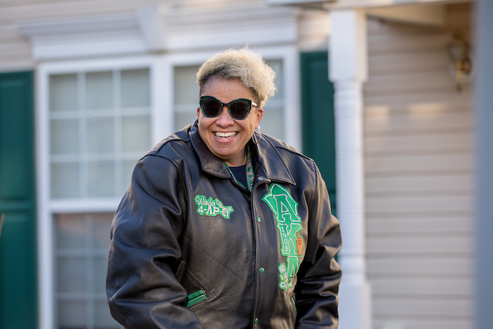 Kathleen smiles wearing a black leather jacket outside her home.