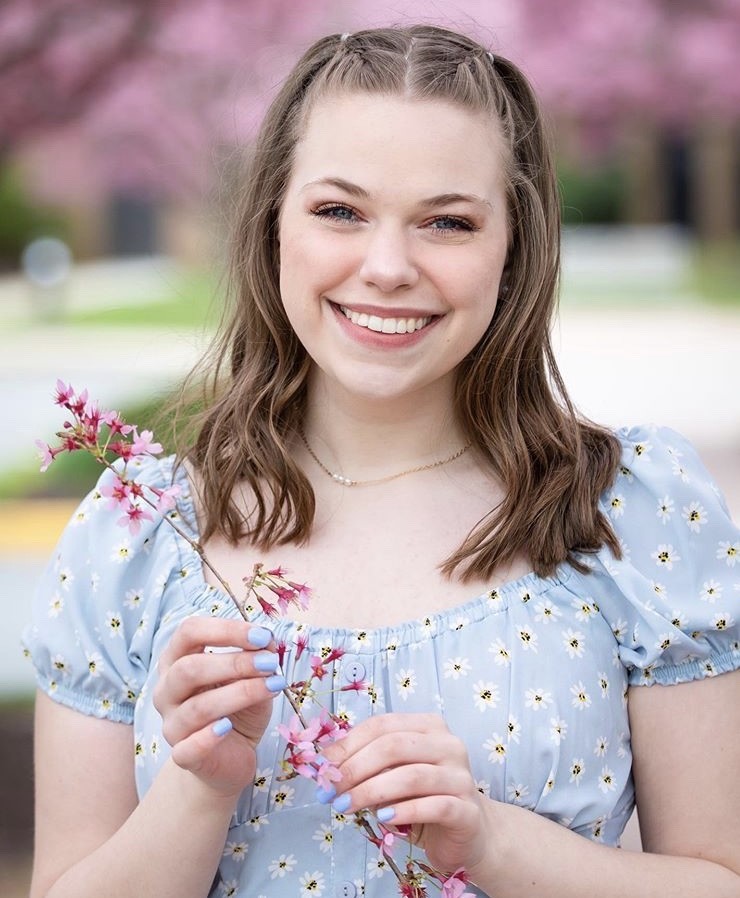 A portrait of Paige smiling and holding a pink flower.