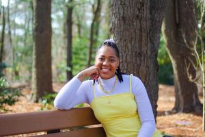 Ayanna wearing a yellow dress while sitting on a bench and smiling.