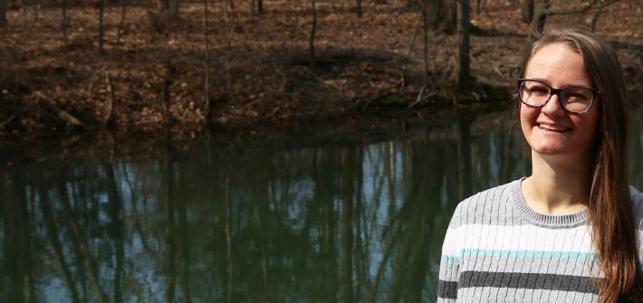 Allison stands and smiles next to a waterway on campus.
