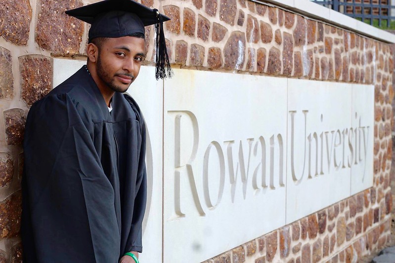 Student standing in front of the Rowan stone sign.
