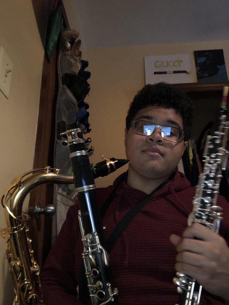 Selfie of Isaiah with a saxophone and two clarinets.