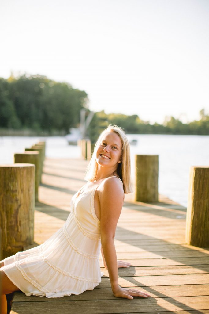 Abby sitting on a dock with a white dress on.