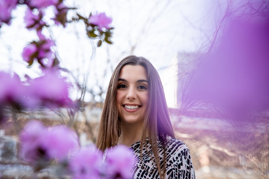 Loredonna smiles behind purple springtime flowers on campus.