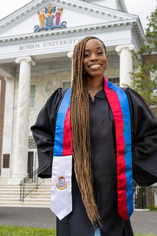 Esther smiles wearing her graduation gown with Bunce Hall in the background.