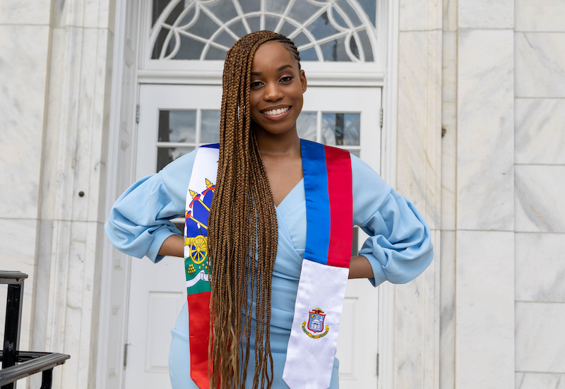 Esther stands and smiles in front of an entrance door at Bunce Hall.