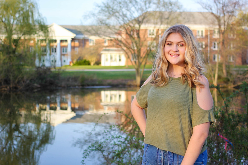 Caroline smiles and poses by a pond overlooking Chestnut Hall.