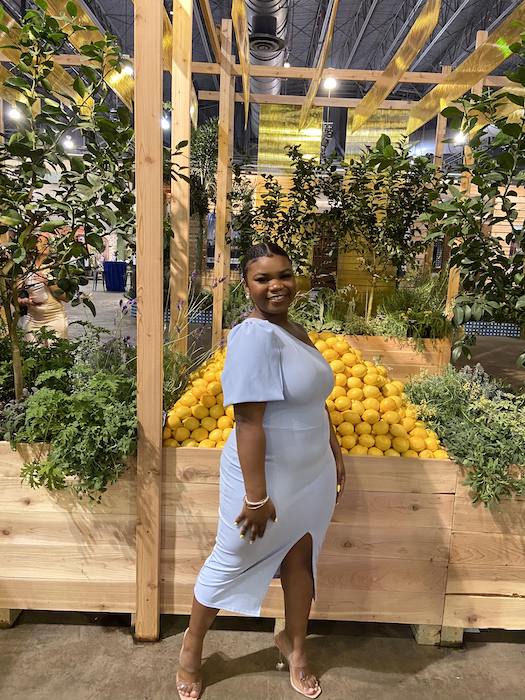 Dyone poses by a pile of lemons and hanging plants at the Philadelphia Garden Convention, wearing a lovely baby blue dress.