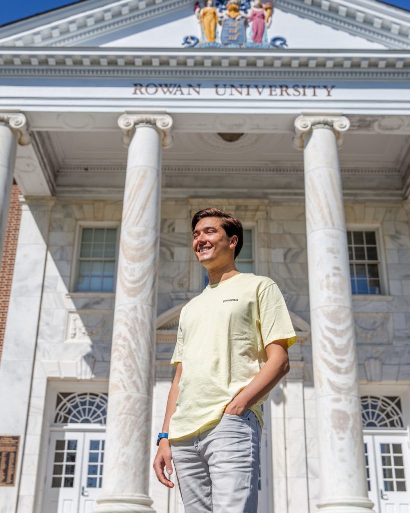 Anthony gazes into the sun in front of Bunce Hall wearing all light colors.