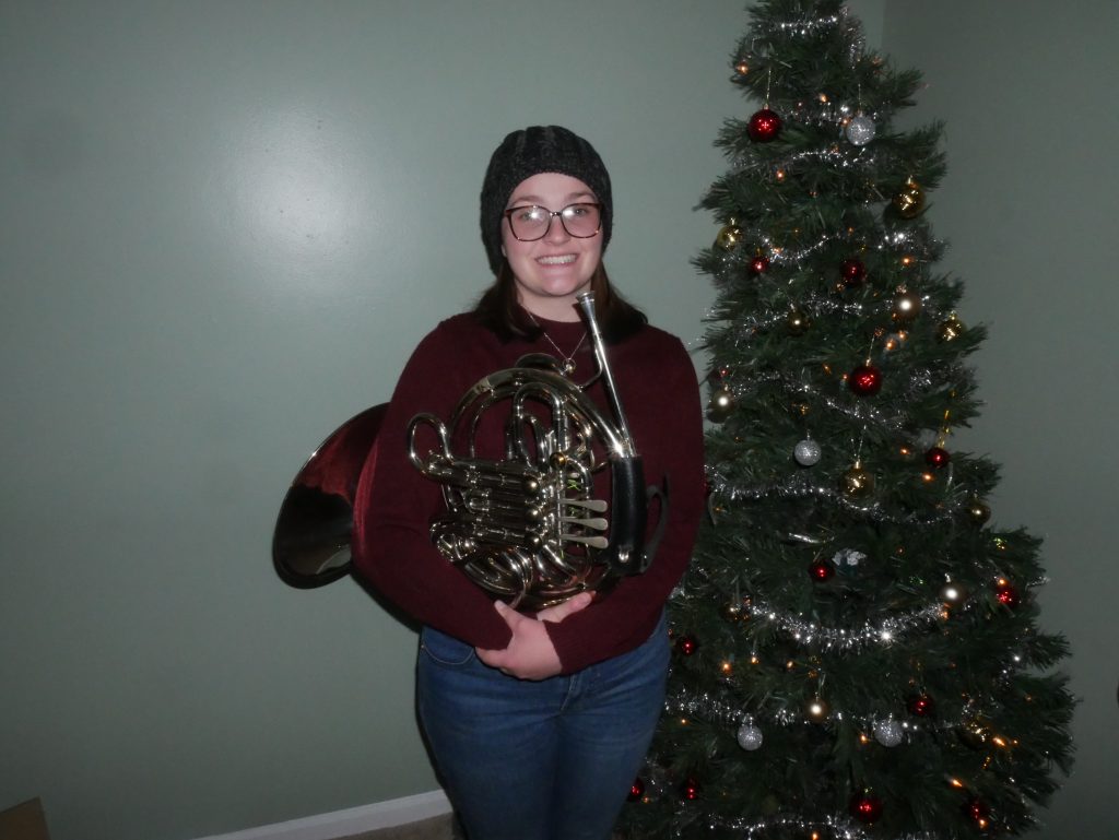 Abby smiling with French horn in front of Christmas tree.