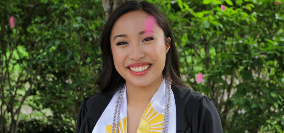 Marian poses in front of a bush with her graduation regalia.