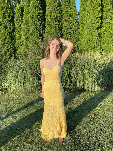 Stephanie smiles outside wearing a yellow dress.