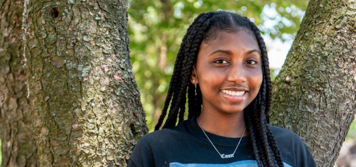 Nene smiles in front of a tree on campus.