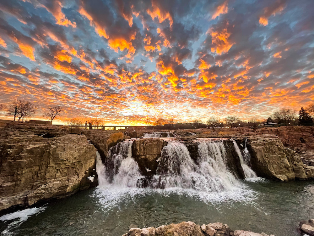 A gorgeous blue and orange sunset shines above a majestic waterfall in Minnesota.