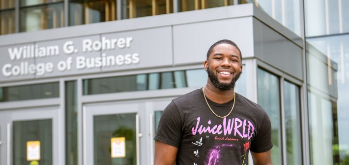 Reshaun smiles and stands in front of the entrance to Business Hall.