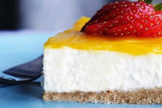 Close up of a slice of white cheesecake with lemon yellow glaze and a strawberry.