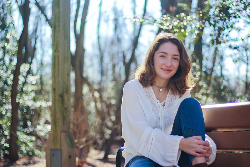 Sarah poses on a bench by trees near Rowan Hall.