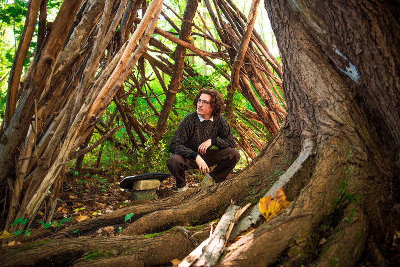 Brandon crouches in a wooded area of campus.