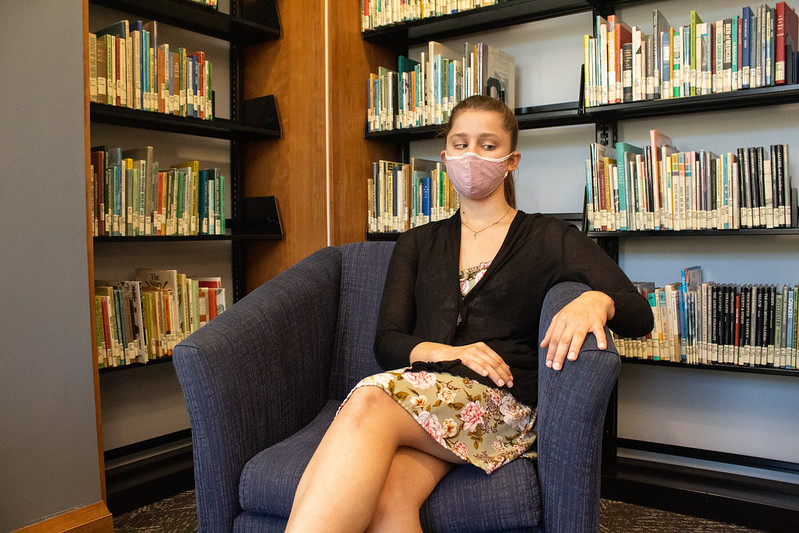 Brianna sits in the Campbell Lbrary, in front of book stacks, on Rowan's campus.