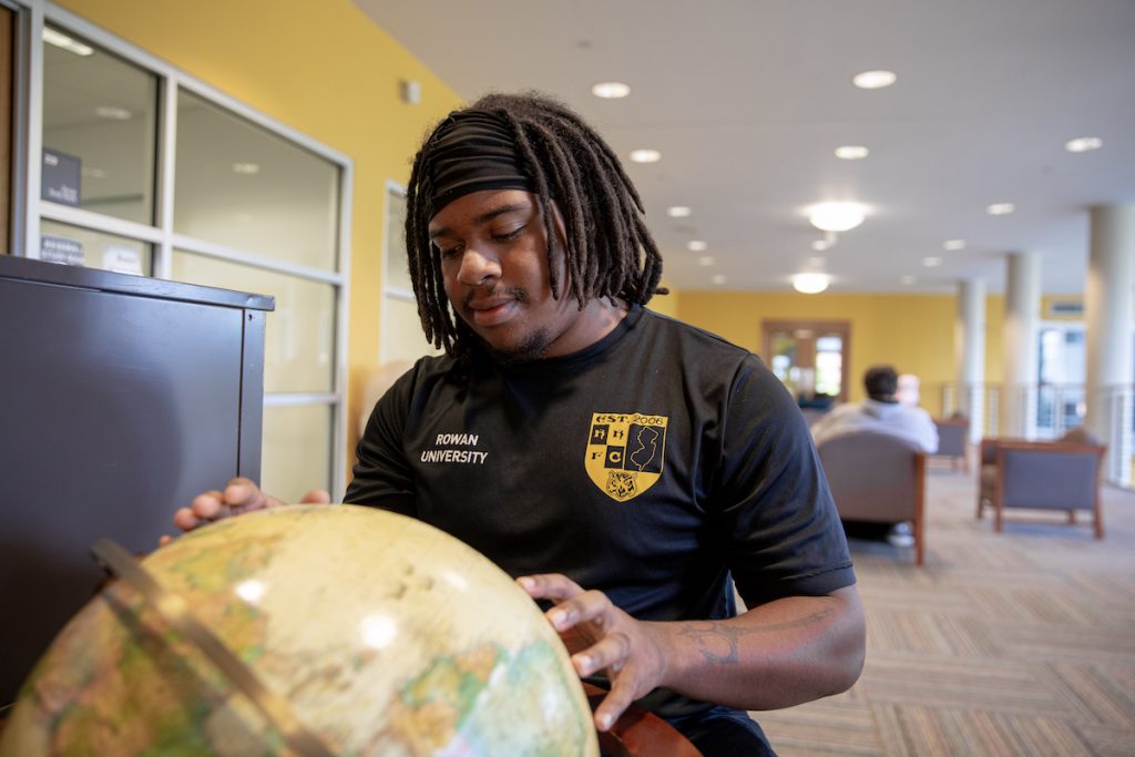 Jaylen, a Rowan University geography major, looks at a globe.