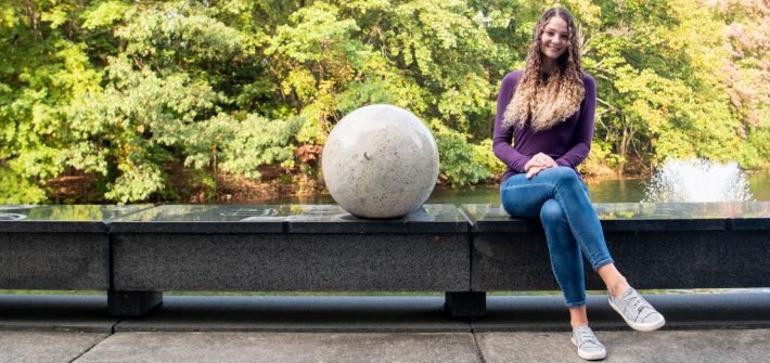 Lauren sits on a bench next to a white, sphere sculpture.