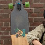 Maria sits with her longboard in front of a brick building on campus.