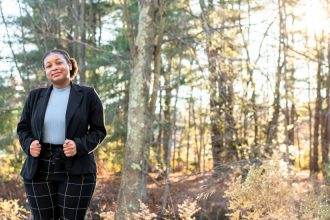 Tiana poses in front of a wooded area.