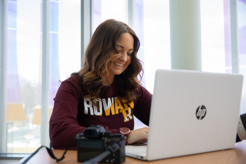 Ashley works on a laptop with her camera at her side inside Business Hall.