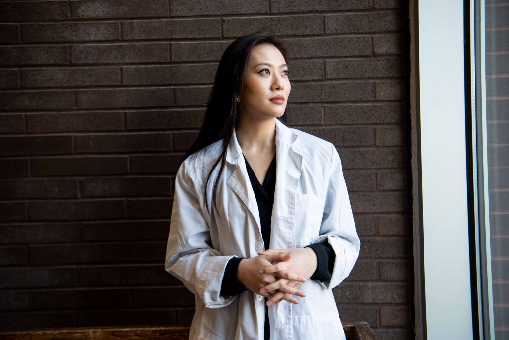 Terry wears a white coat while looking out a large window.