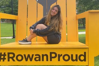 Valentina poses on the #RowanProud chair near Bunce Hall.