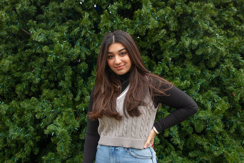 Rohama Dada stands in front of some shrubbery on Campus while smiling directly at the camera.
