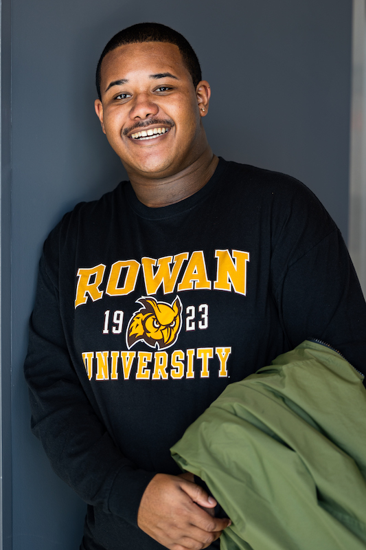 Jamar smiles wearing a Rowan shirt and hold a green jacket on his arm.