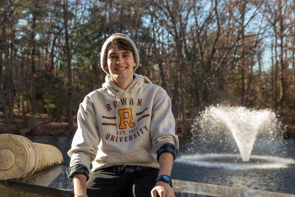Connor smiles in front of a fountain by the engineering pond.