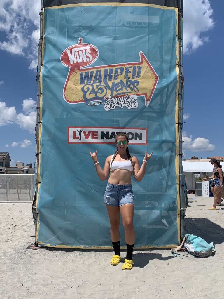 Emileigh is standing out front of a sign at Warped Tour. 