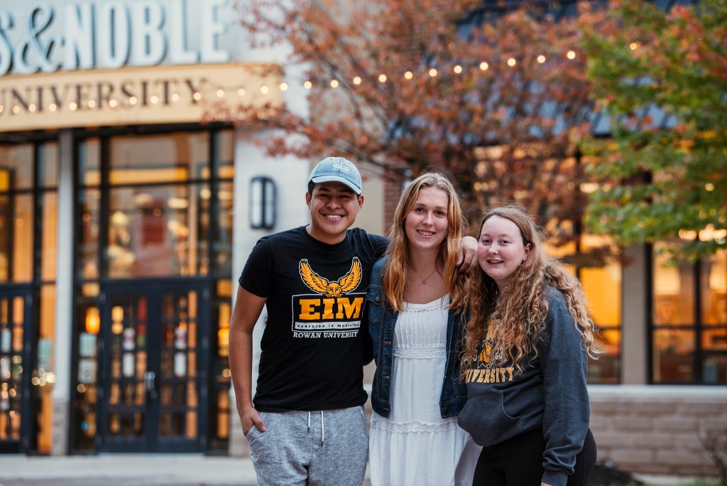 Three smiling students by the bookstore.