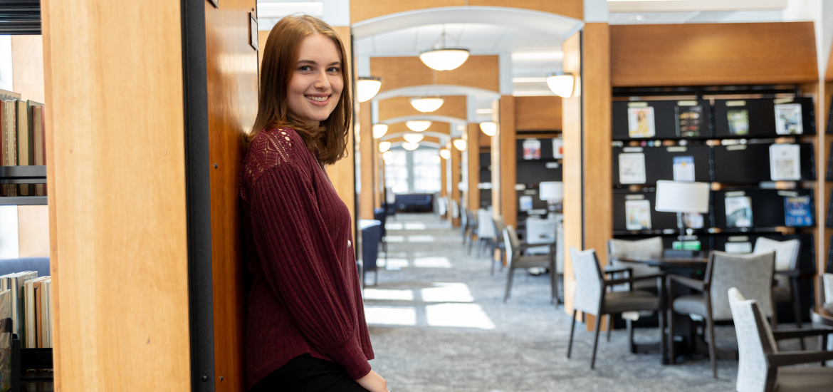 Jessica Newell smiles and stands inside the Chamberlain Library.
