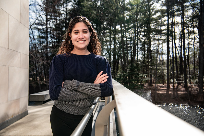 Maria is leaning against a railing with her arms crossed. 