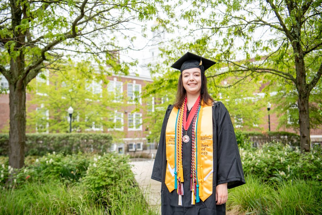 Sarah stands in a garden in her cap and gown.