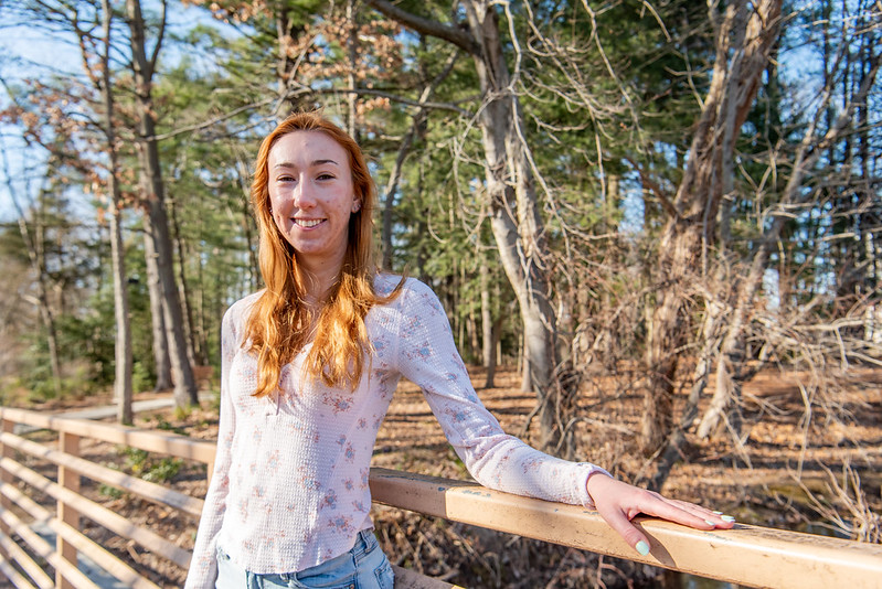 Leah is leaning against a wooden fence and smiling at the camera.